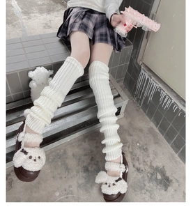 Close-up of white cable-knit leg warmers with a pleated skirt and platform shoes