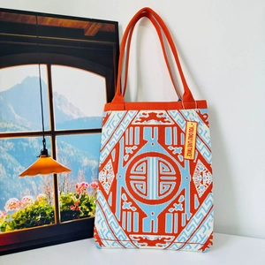 Close-up of geometric knit tote bag in orange and blue with YOU ONLY LIVE TWICE tag