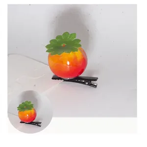 Detail view of a 3cm tomato-shaped hair clip with vibrant red finish and green leaves
