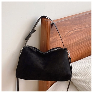 Close-up of black suede shoulder bag with silver hardware on a wooden bedframe