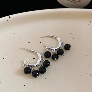 Elegant silver tassel earrings with glossy black beads on a minimalist ceramic display