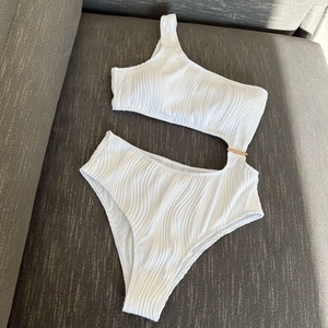 Detail of white one-shoulder monokini featuring ribbed texture and gold buckle hardware