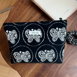 Détail de la broderie papillon et étiquette Simple Wish sur la trousse en toile noire