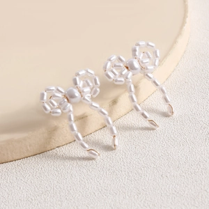 Detailed view of handmade bow-shaped pearl earrings with gold accents on a display