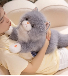 Gros plan d'une peluche de chat à poils longs gris et blanc tenue par un mannequin sur un canapé