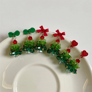 Detail of beaded Christmas tree earrings with red bows and hearts on a ceramic plate