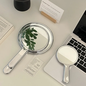 Detail of silver handheld mirrors in two sizes with a sleek chrome finish on a desk