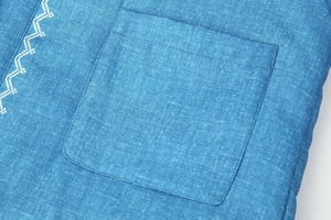 Dettaglio giacca vintage in cotone denim con tasca quadrata e ricamo geometrico bianco