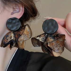 Close-up of vintage black metal and golden jacquard fabric petal earrings worn by a model