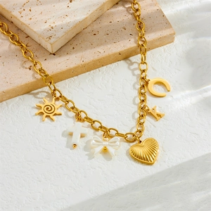 Retro gold chain necklace with heart, bow, and cross charms on a textured stone base