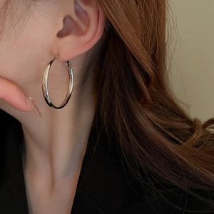Close-up of a model wearing large silver hoop earrings with a polished metallic finish