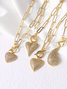 Close-up of gold chunky necklaces with heart pendants and sparkling zircon inlays with OT clasp