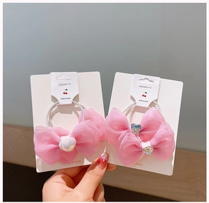 Close-up of pink mesh bow hair clips with heart pearl charms on a white display card