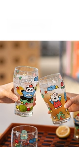 Detail showing two hands clinking 600ml cartoon glass cups in a warm home setting
