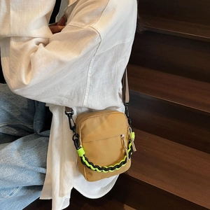 Detail view of khaki canvas crossbody bag with neon green cord and adjustable brown strap