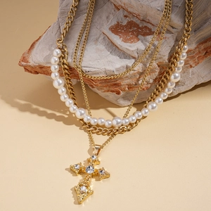 Close-up of multilayer gold Cuban chain with pearl beads and rhinestone cross pendant