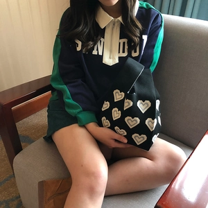 Close-up of black knitted tote bag with blue heart pattern held by a model on a sofa
