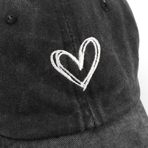 Close-up of heart embroidery on washed black cotton baseball cap with twill texture