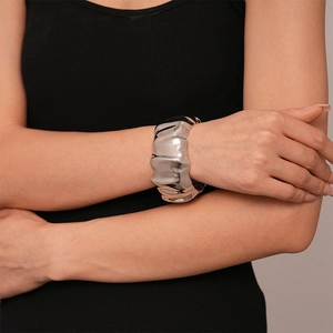 Close-up of a silver-tone wide cuff bracelet with a rippled metallic texture on woman wrist