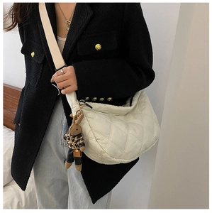 Side view of white quilted shoulder bag with rabbit charm worn by a model