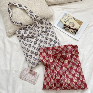 Close-up of floral canvas tote bags in blue and red patterns on a soft fabric surface