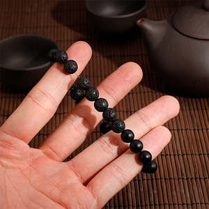 Macro shot of lava stone and matte black beads on an elastic bracelet held by hand