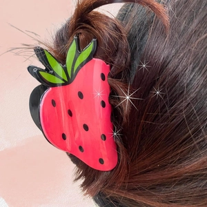 Detailed view of a cute red strawberry hair claw clip worn on long brown hair