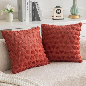 Detail of two rust red plush pillow covers with textured 3D heart jacquard patterns