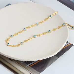 Detail of golden butterfly chain and blue Evil Eye beads on a ceramic plate