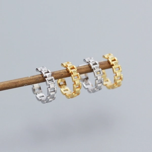 Detail view of silver and gold chain-link ear cuffs on a minimalist brown display rod
