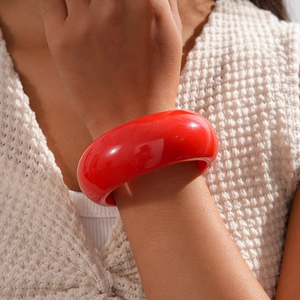 Close-up of a wide red resin bangle on a wrist showing high-gloss finish and round shape
