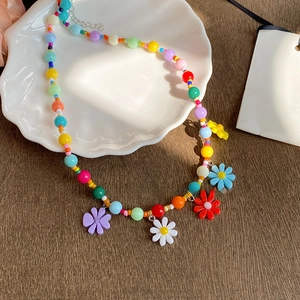 Colorful beaded daisy necklace with vibrant floral charms on a white ceramic tray