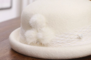 Detailed macro view of wool felt hat with white faux fur pom poms and mesh lace trim