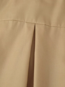 Détail macro du tissu plissé kaki avec coutures précises sur un ensemble haut et jupe