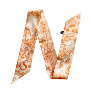 Close-up of a cream narrow twilly silk scarf featuring orange tropical palm and letter S