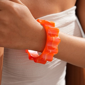 Macro shot of a chunky scalloped acrylic bangle featuring orange marbled textures