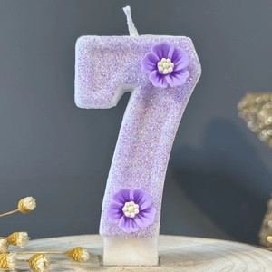 Glittery purple number 7 birthday candle with floral decor on a wooden base