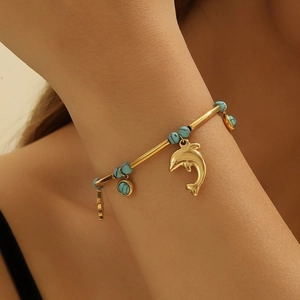 Bracelet chaîne en or avec perles de turquoise et pendentif dauphin porté au poignet