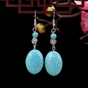 Detail of vintage turquoise drop earrings hanging against a traditional floral backdrop