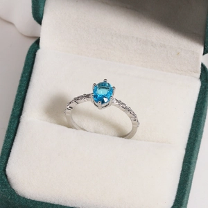 Close-up of oval blue zircon ring in silver setting on green velvet display case