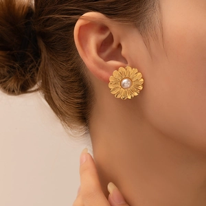 Elegant gold daisy earrings with pearl center inlay shown on a model in warm light