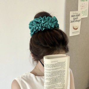 Detail of peacock green satin hair scrunchie with pleated texture on model's hairstyle