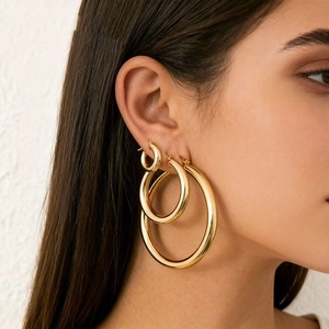 Three pairs of polished gold stainless steel hoop earrings in various sizes on model