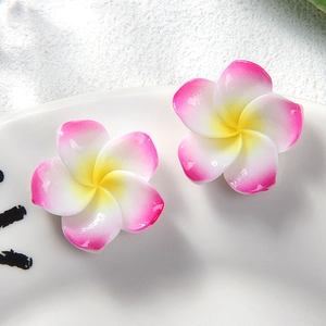 Detail shot of two pink and white resin frangipani earrings on a white ceramic tray