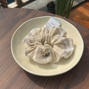 Beige linen texture scrunchie with shell and pearl accents on a ceramic plate