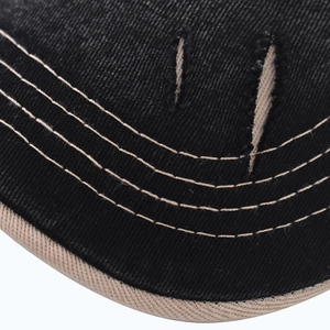 Macro detail of black denim fabric featuring beige contrast stitching and vintage distressed holes