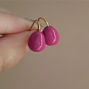 Detail shot of fuchsia water drop earrings with elegant gold hooks held in hand