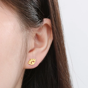 Gros plan d'une boucle d'oreille œil du démon dorée portée par un mannequin pour un look chic