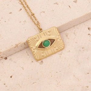 Macro shot of gold Evil Eye rectangle pendant with green gemstone on stone background