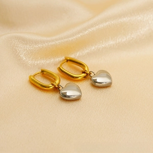 Detailed view of two-tone heart dangle earrings on elegant gold silk fabric background